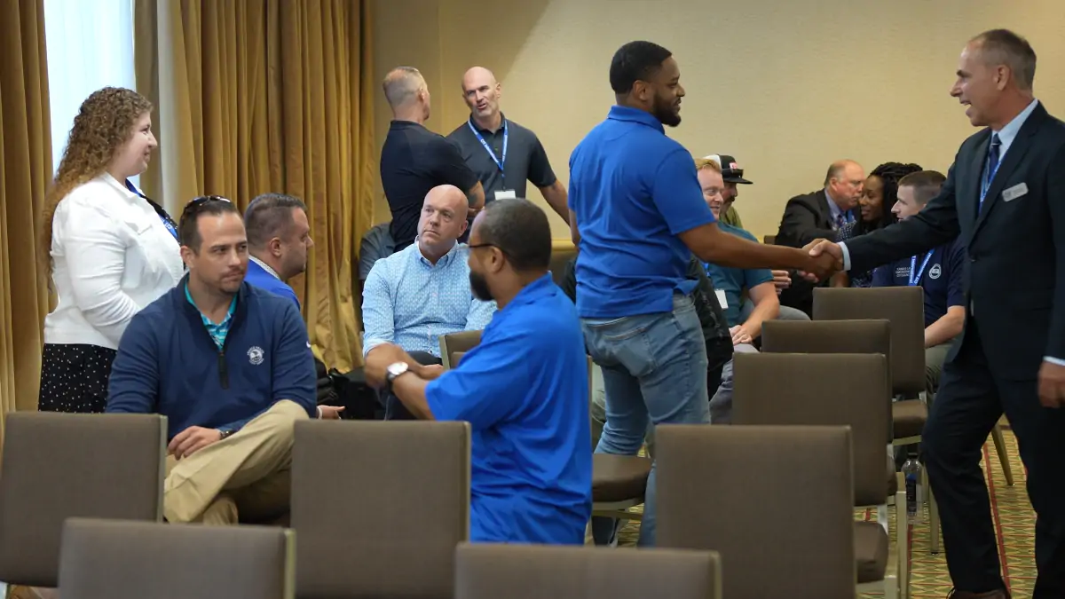 Several Community of Practice members seated and standing greeting one another in a conference room.